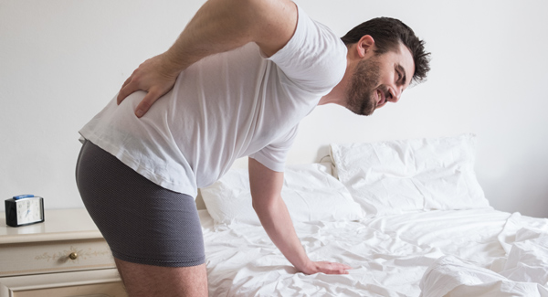 man waking up with back pain pressing down on mattress
