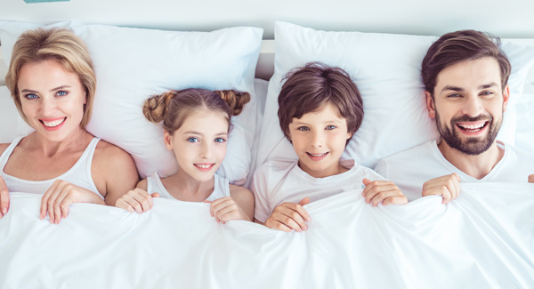 happy young couple sharing a large bed with their two children