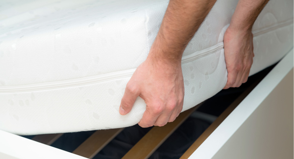 Man lifting a mattress off white bed frame with hands