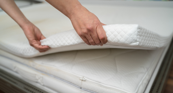 Lady lifting mattress topper off bed