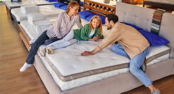 Happy young family sitting and lying on a mattress in a showroom