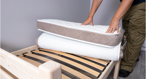 Man unrolling new mattress on slatted bed frame
